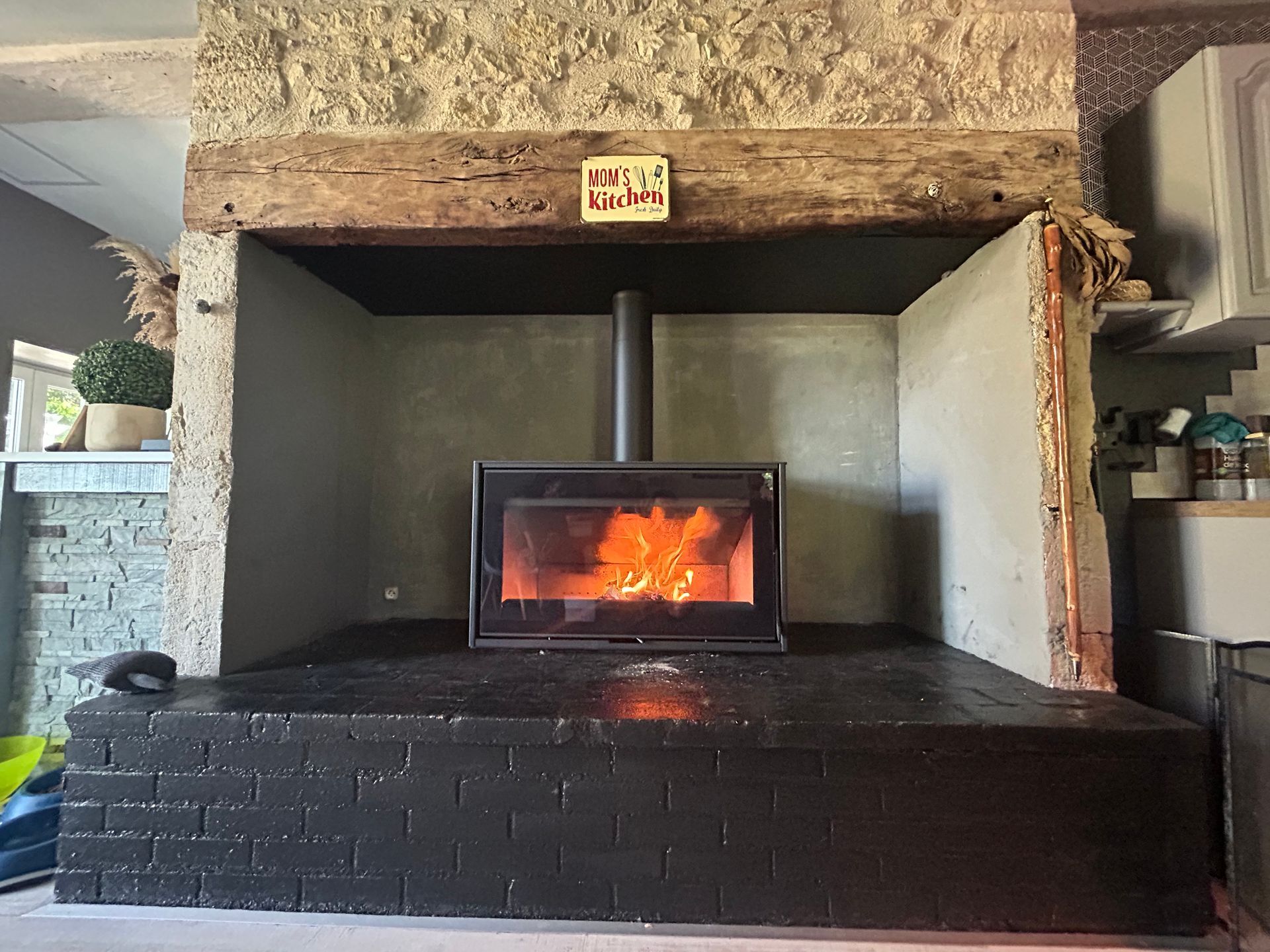 Cheminée avec feu brûlant à l'intérieur, entourée de briques noires et d'un manteau en pierre