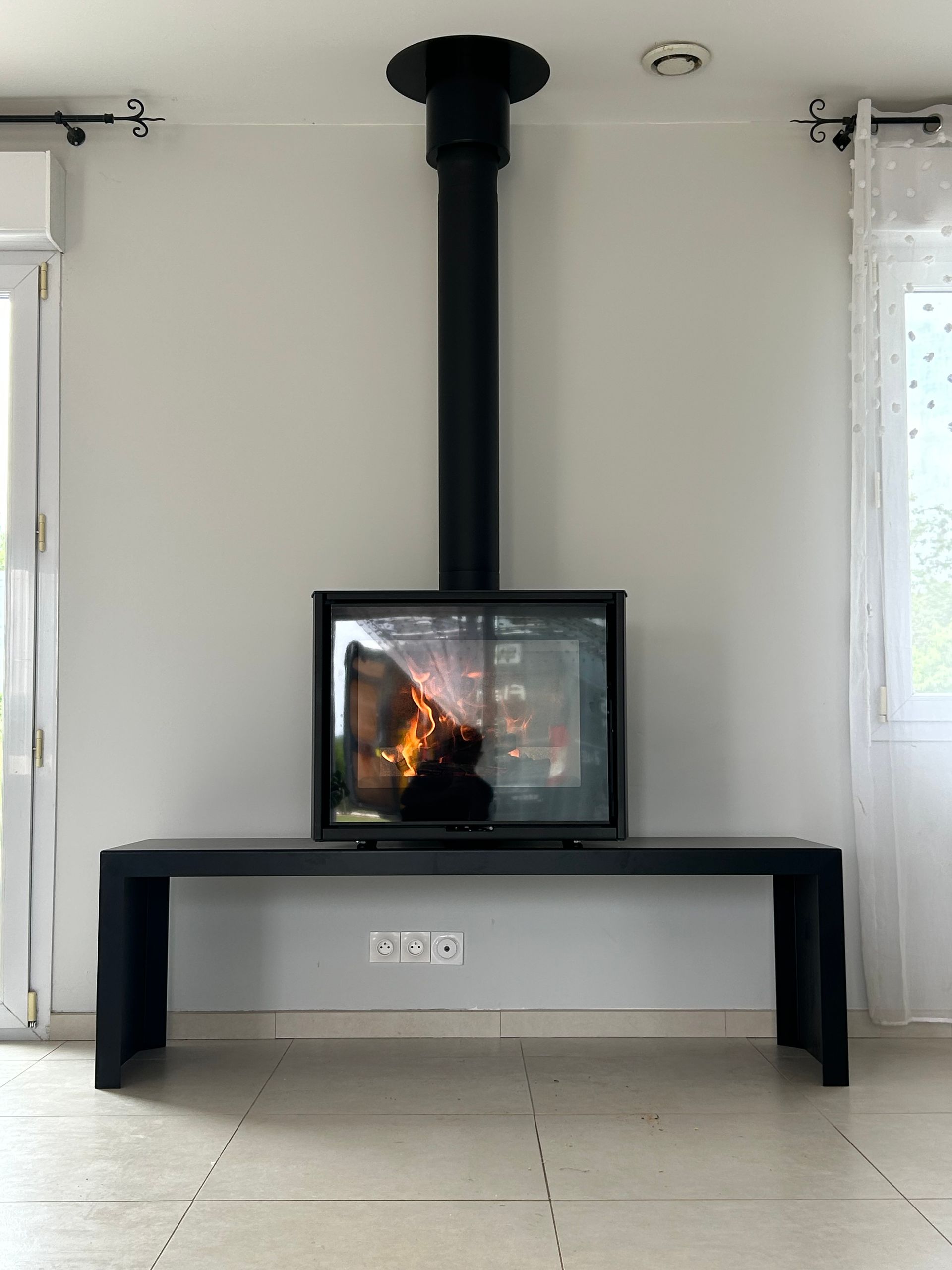 Cheminée noire suspendue au dessus d'un banc noir, montée sur un mur blanc