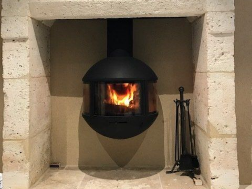 Un poêle à bois noir et sphérique aux flammes visibles est suspendu dans une cheminée en pierre