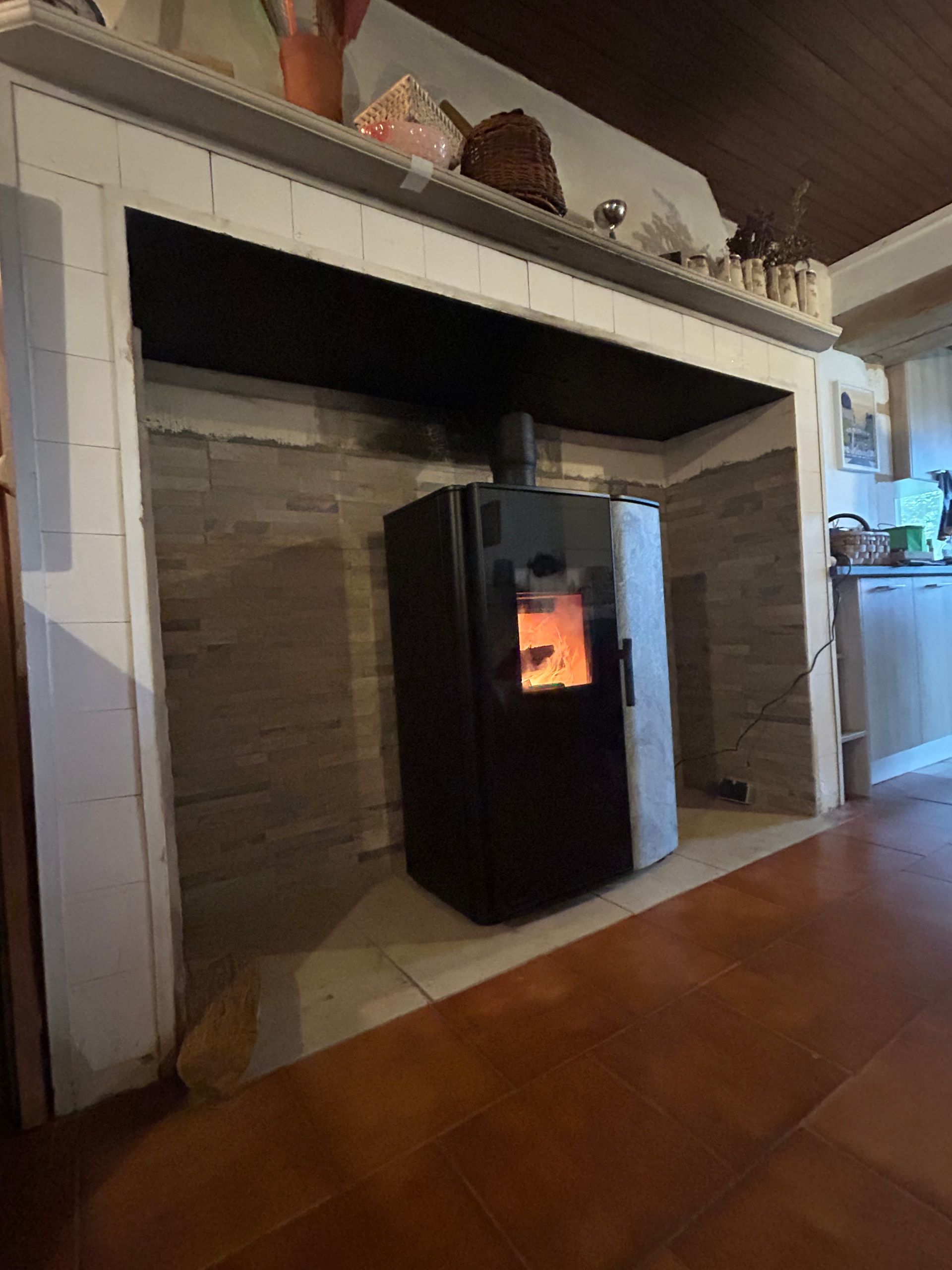 Poêle à bois noir dans une cheminée en pierre, sol marron, garnitures blanches