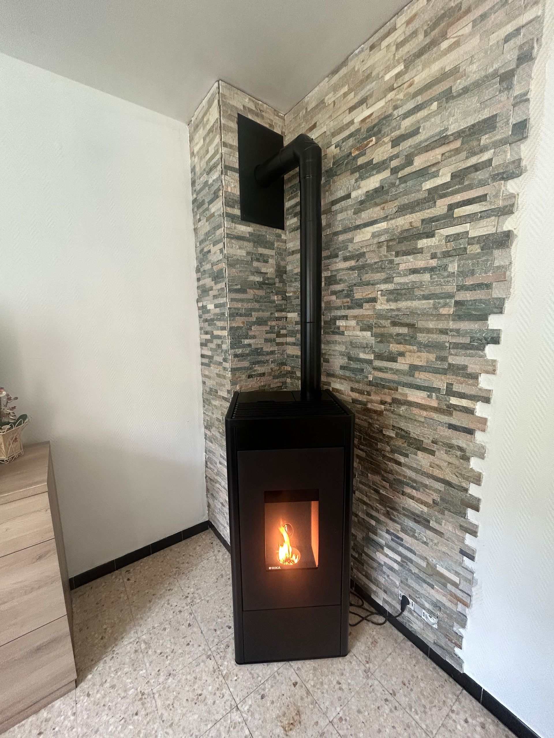 Cheminée noire avec des flammes brûlant contre un mur de pierre dans un coin d'une pièce