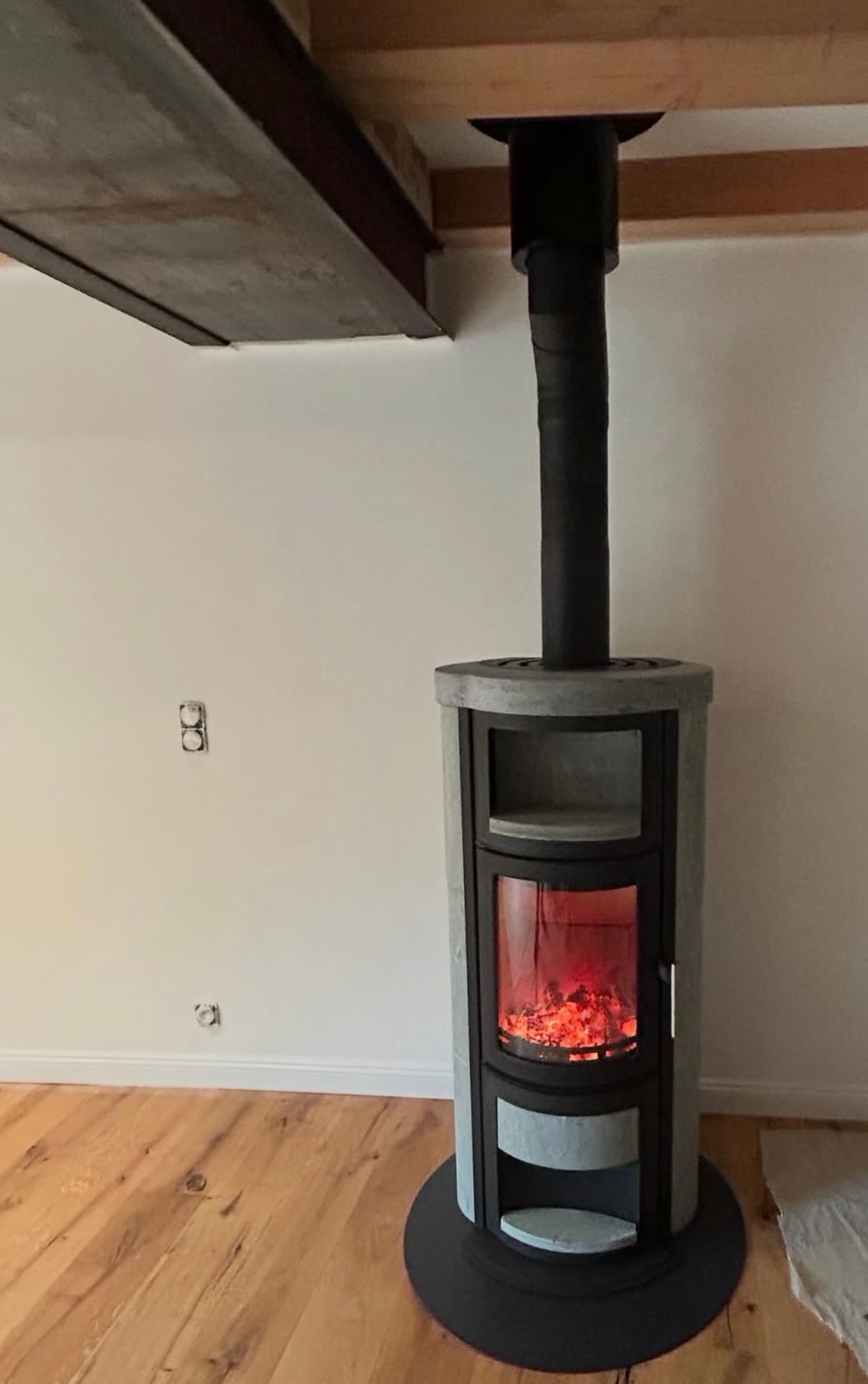 Poêle à bois avec un feu rougeoyant, entouré de pierre grise, contre un mur blanc avec une cheminée noire