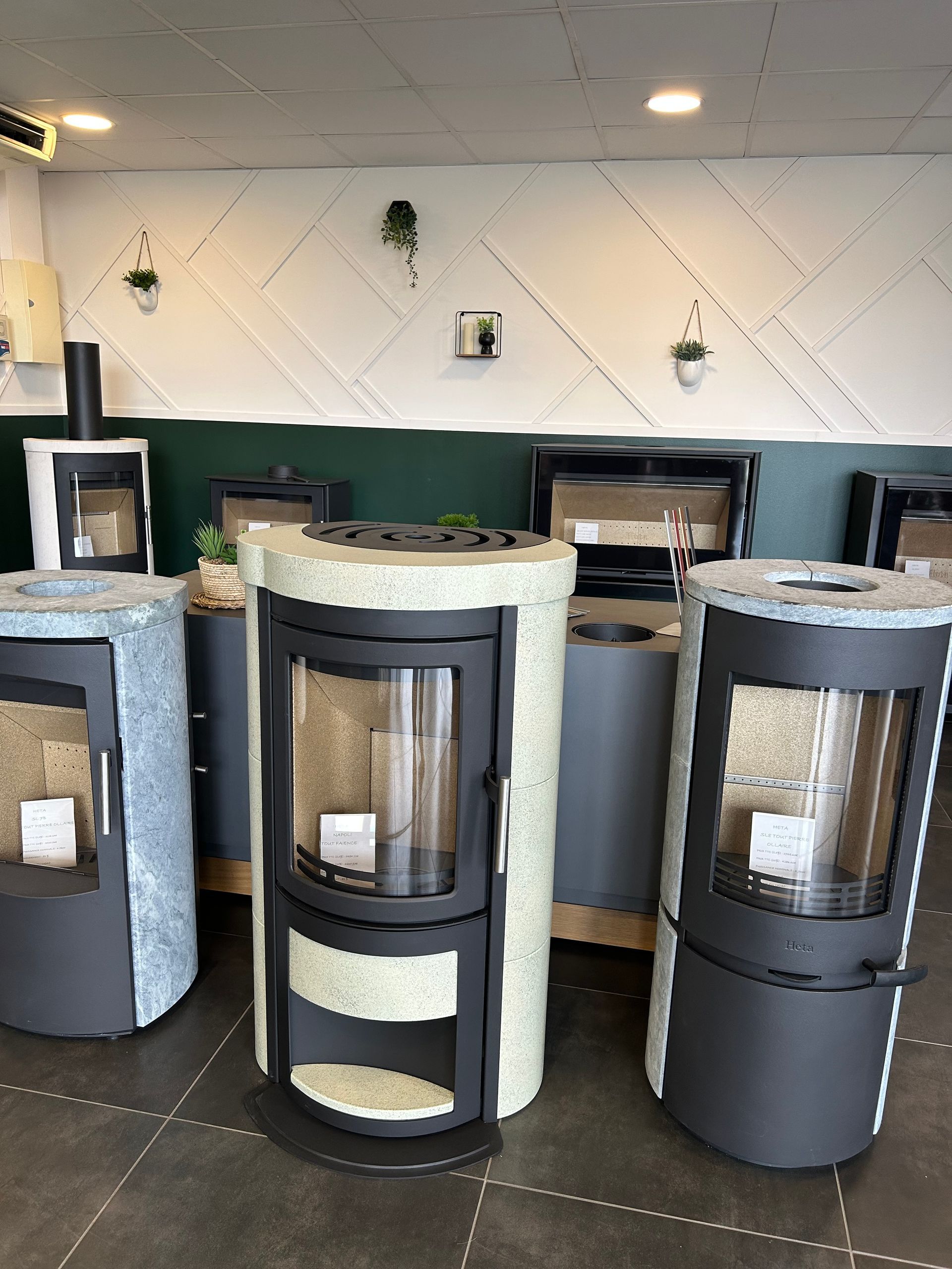Poêles à bois dans une salle d'exposition aux designs et couleurs variés, contre un mur blanc et vert