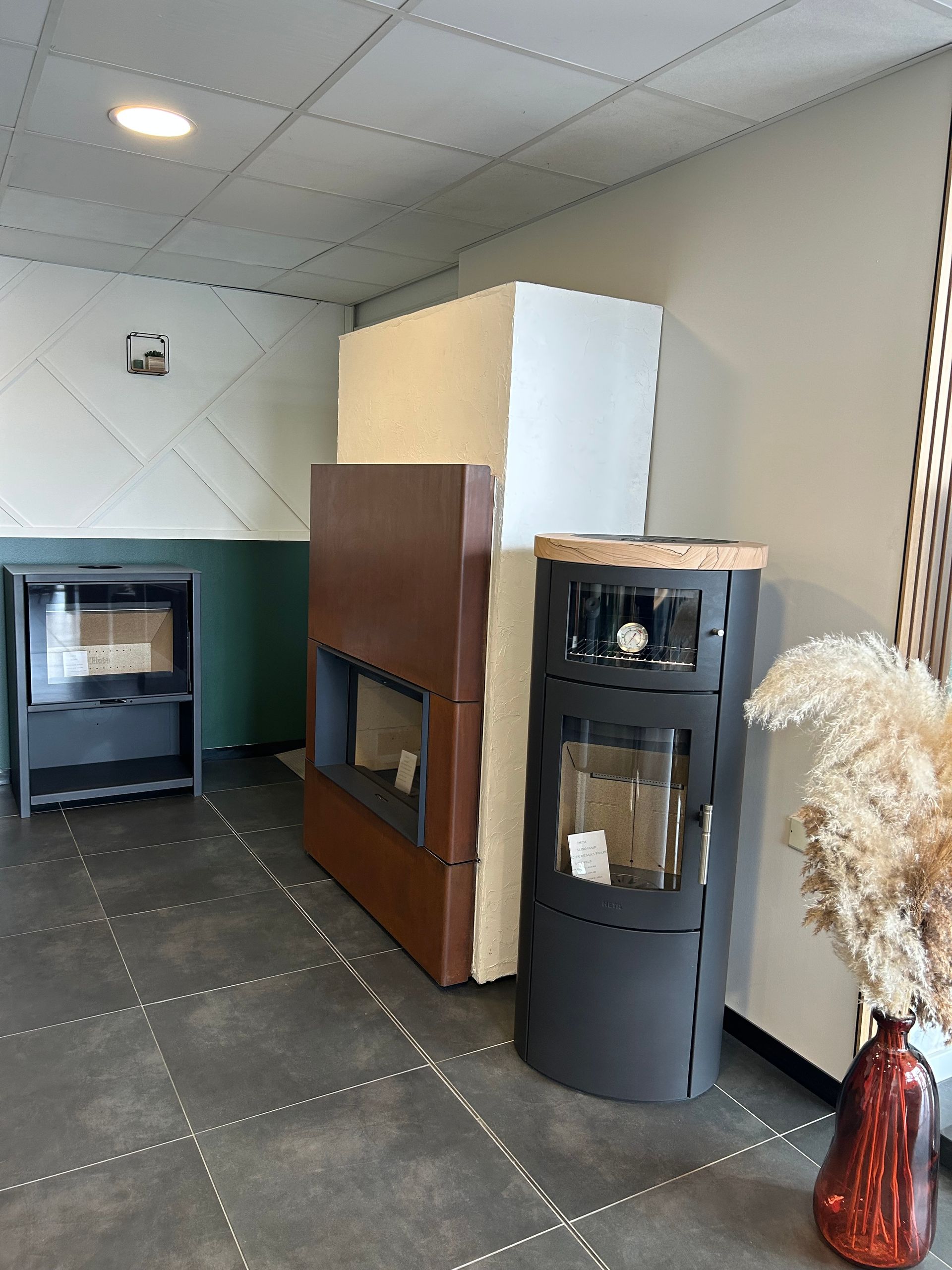 Showroom de cheminées : Différents modèles de cheminées exposés, sol en carrelage gris, murs neutres et plantes décoratives