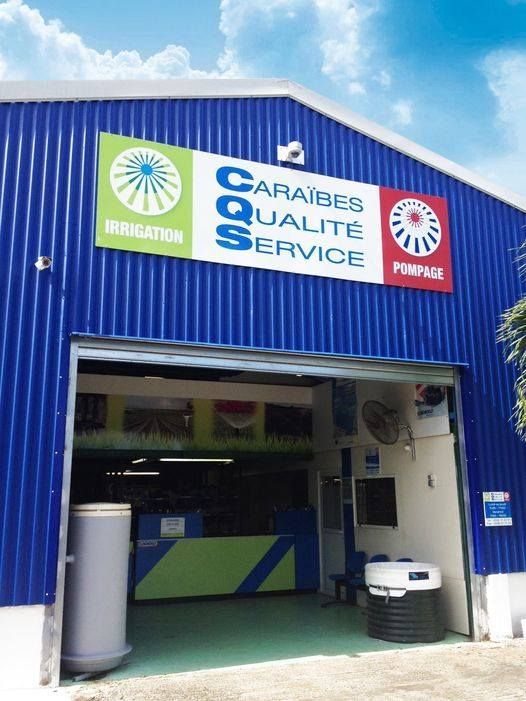 Bâtiment bleu avec porte ouverte, panneau Caraïbes Qualité Service.