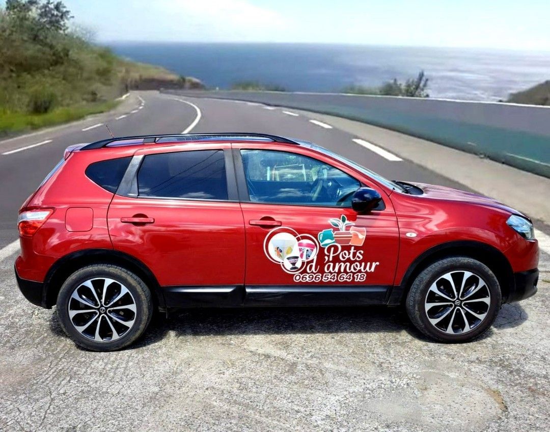Voiture rouge sur une route côtière, océan en arrière-plan.