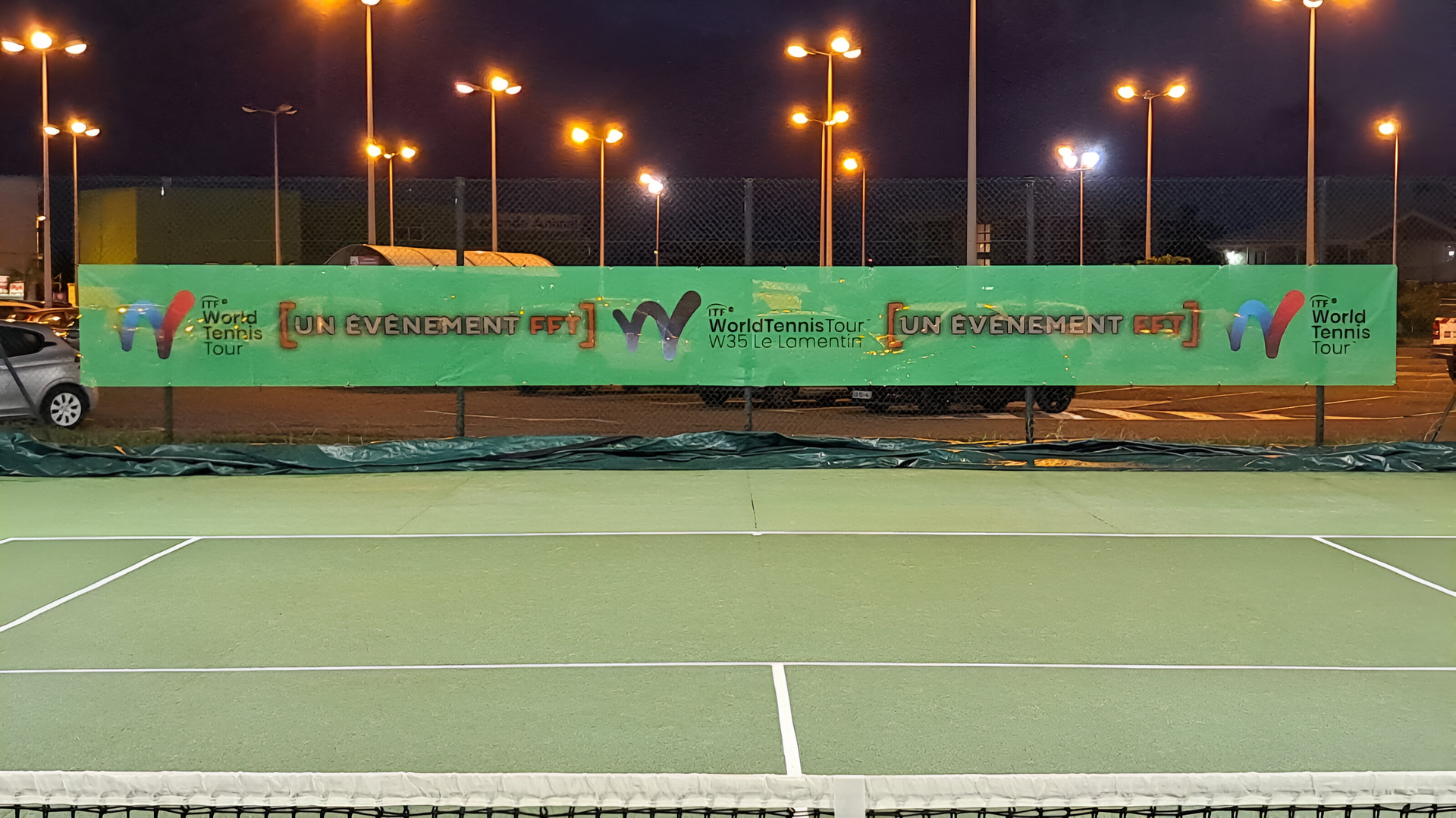 Court de tennis de nuit avec surface verte et banderole verte.