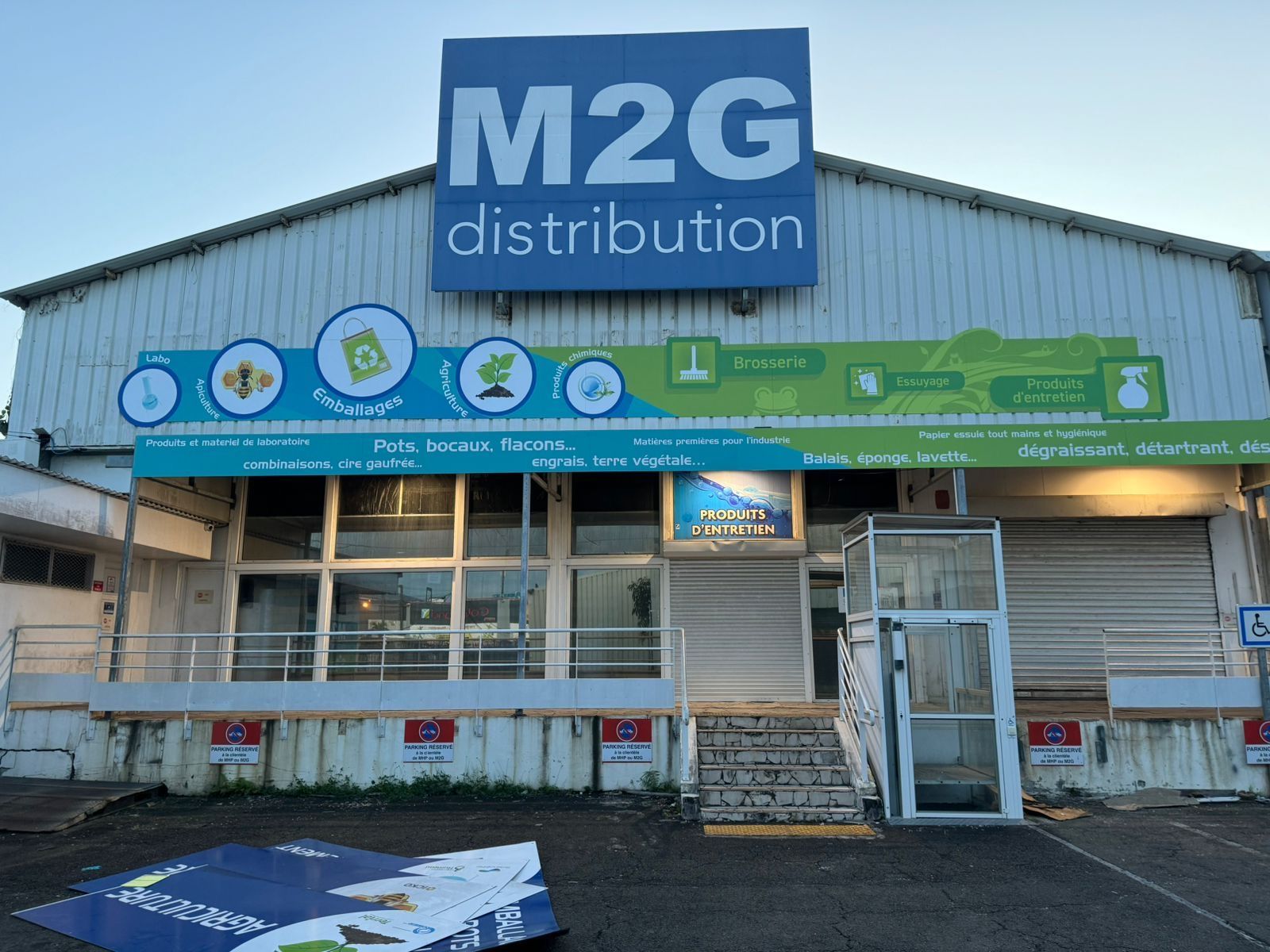 Bâtiment de distribution M2G avec une enseigne bleue et blanche et une rampe d'accès.