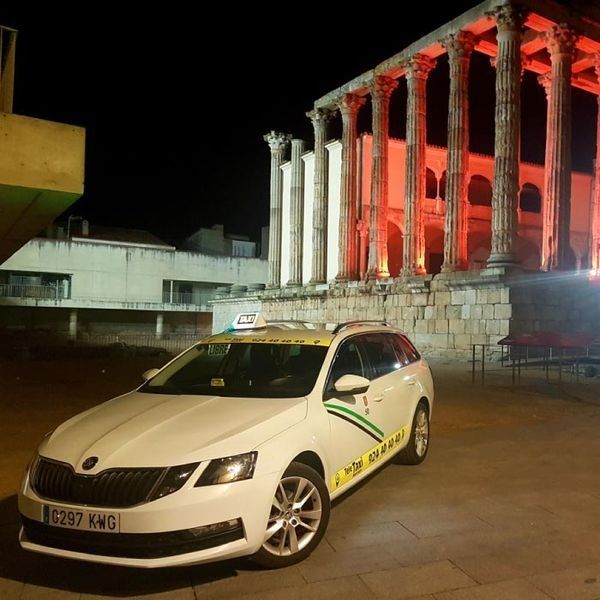 Taxi blanco estacionado frente a un templo romano iluminado con luces rojas por la noche.