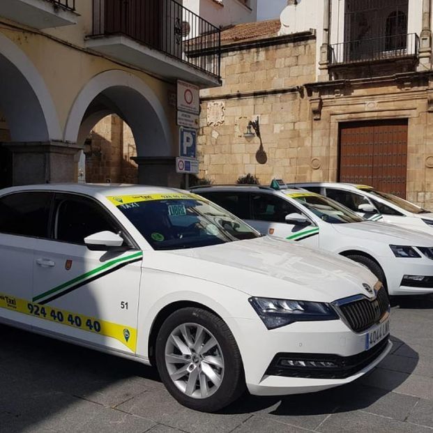 Taxis blancos estacionados frente a un edificio con arcos, número de teléfono en la puerta.
