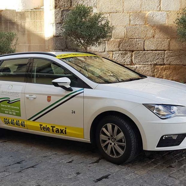 Teletaxi blanco estacionado frente a un edificio de ladrillo, con detalles en verde y amarillo.