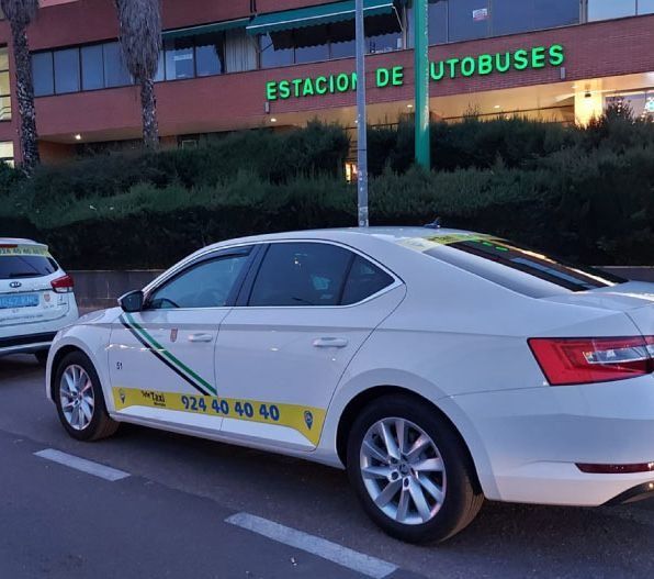 Taxi blanco estacionado frente a una estación de autobuses. Número de teléfono a un lado.