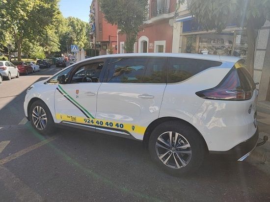 Taxi blanco estacionado en una calle, con una franja amarilla y verde y un número de teléfono.