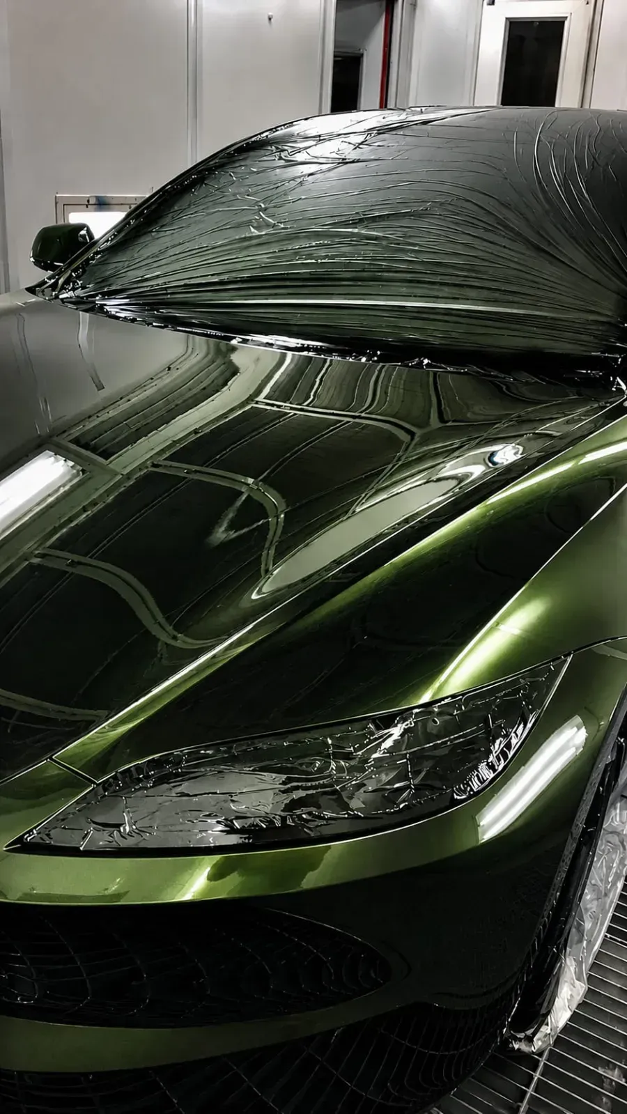 Coche deportivo verde oscuro cubierto de gotas de agua en un garaje o lavadero de coches.