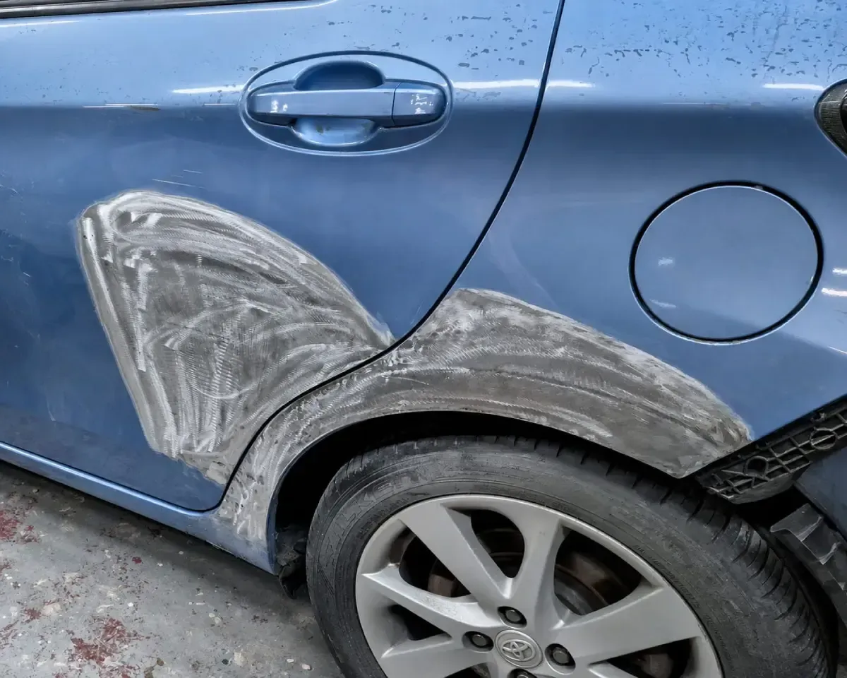 El panel trasero del coche azul presenta arañazos y marcas blancas alrededor del paso de rueda y la puerta.