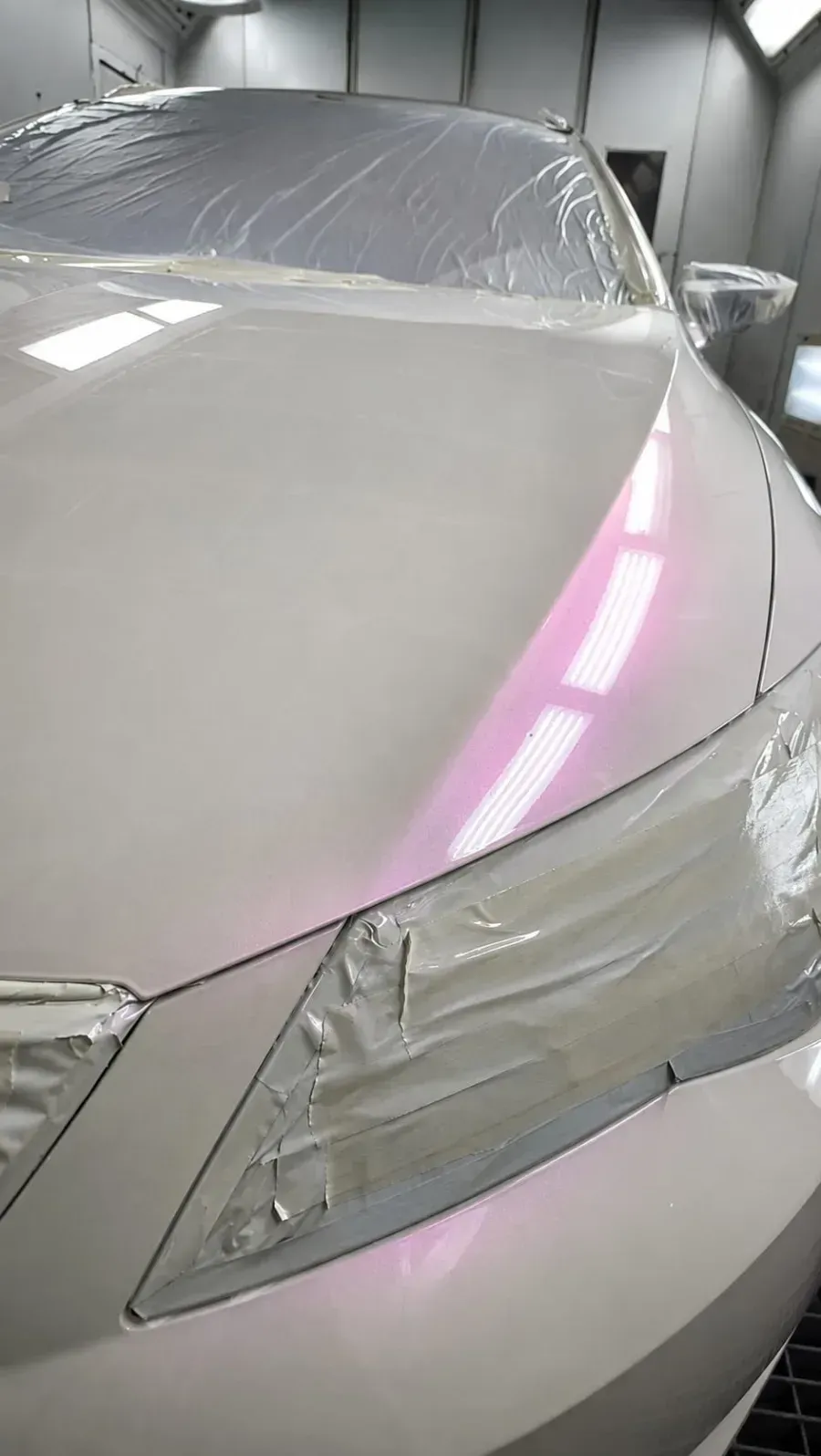 Coche blanco en un taller de chapa y pintura, con el capó y el parabrisas cubiertos con plástico protector.