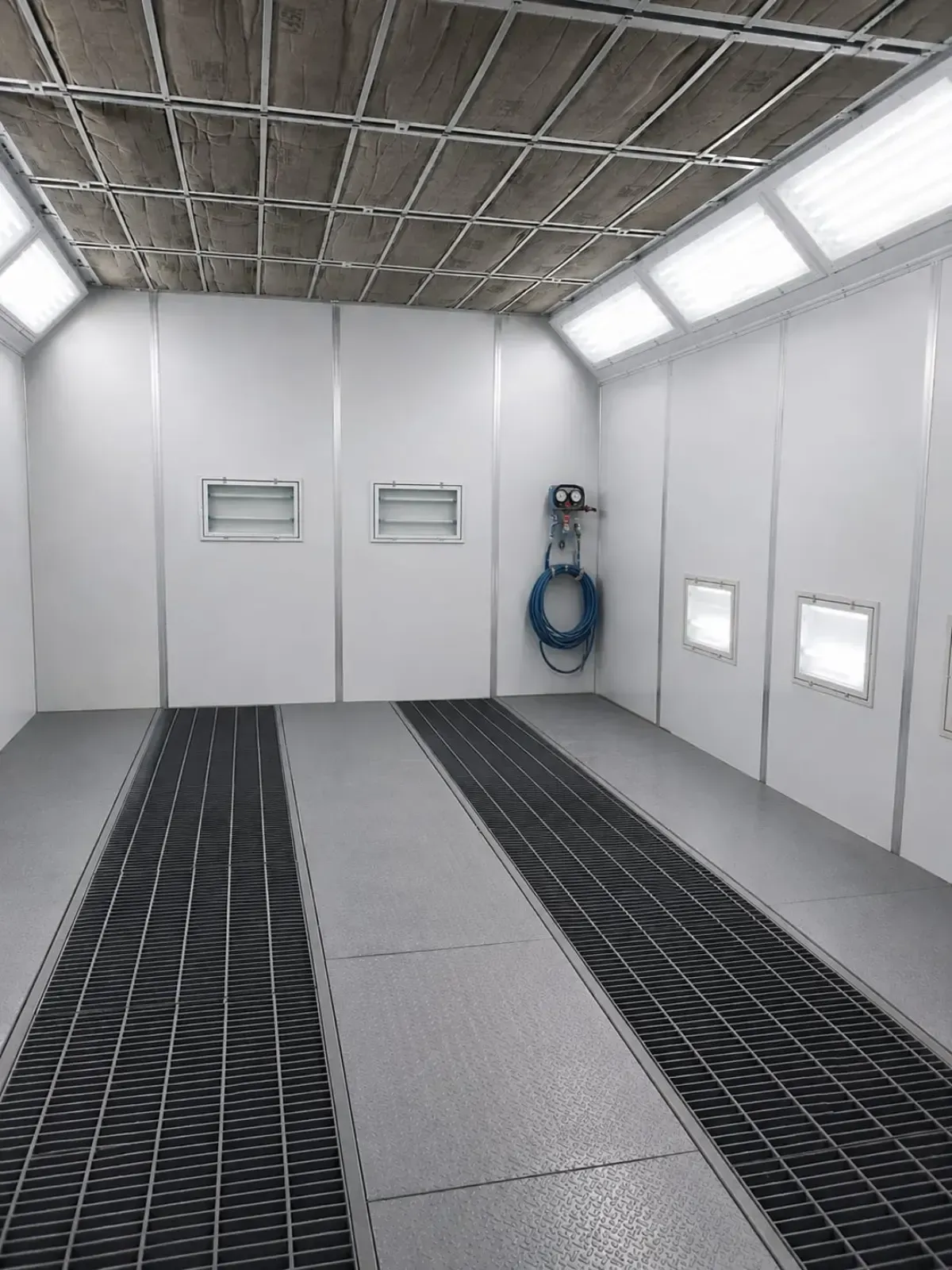 Habitación industrial vacía con paredes blancas, paneles de suelo de rejilla, ventanas y una manguera azul