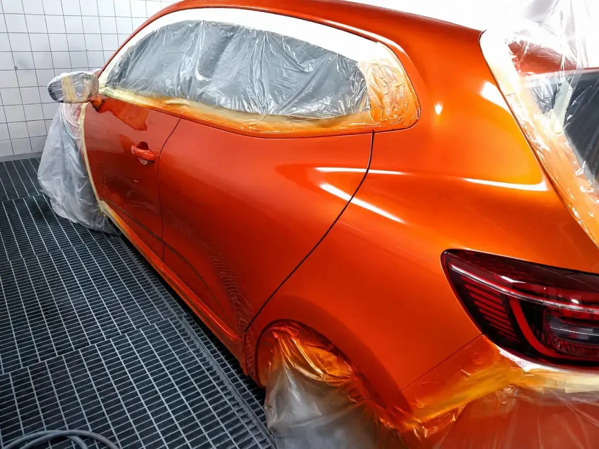 Coche deportivo naranja enmascarado para pintar, cubierto con plástico en un taller de carrocería.