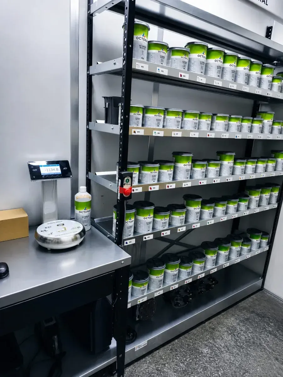 Estantería de laboratorio con filas de frascos de muestra etiquetados y una balanza sobre una mesa de trabajo metálica.