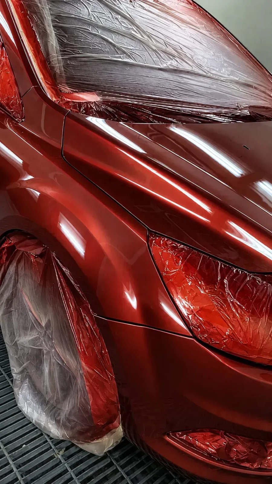 Primer plano de la esquina delantera de un coche rojo brillante con un faro dañado y un panel de la carrocería abollado.