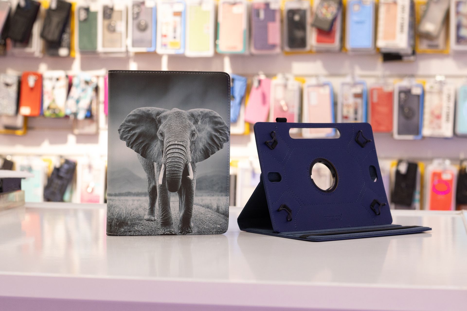 Una funda para tableta con temática de elefante junto a una funda para tableta azul sobre un mostrador blanco