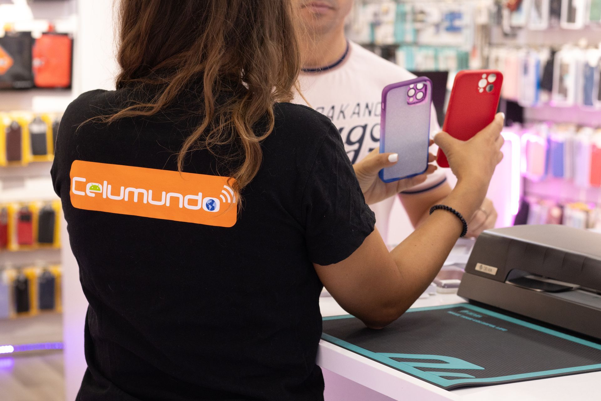Un empleado de Celumundo muestra fundas de teléfono a un cliente en el mostrador de una tienda.