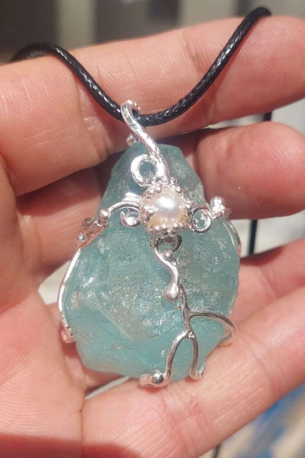 Colgante turquesa envuelto en alambre con un cordón negro, sostenido entre los dedos.