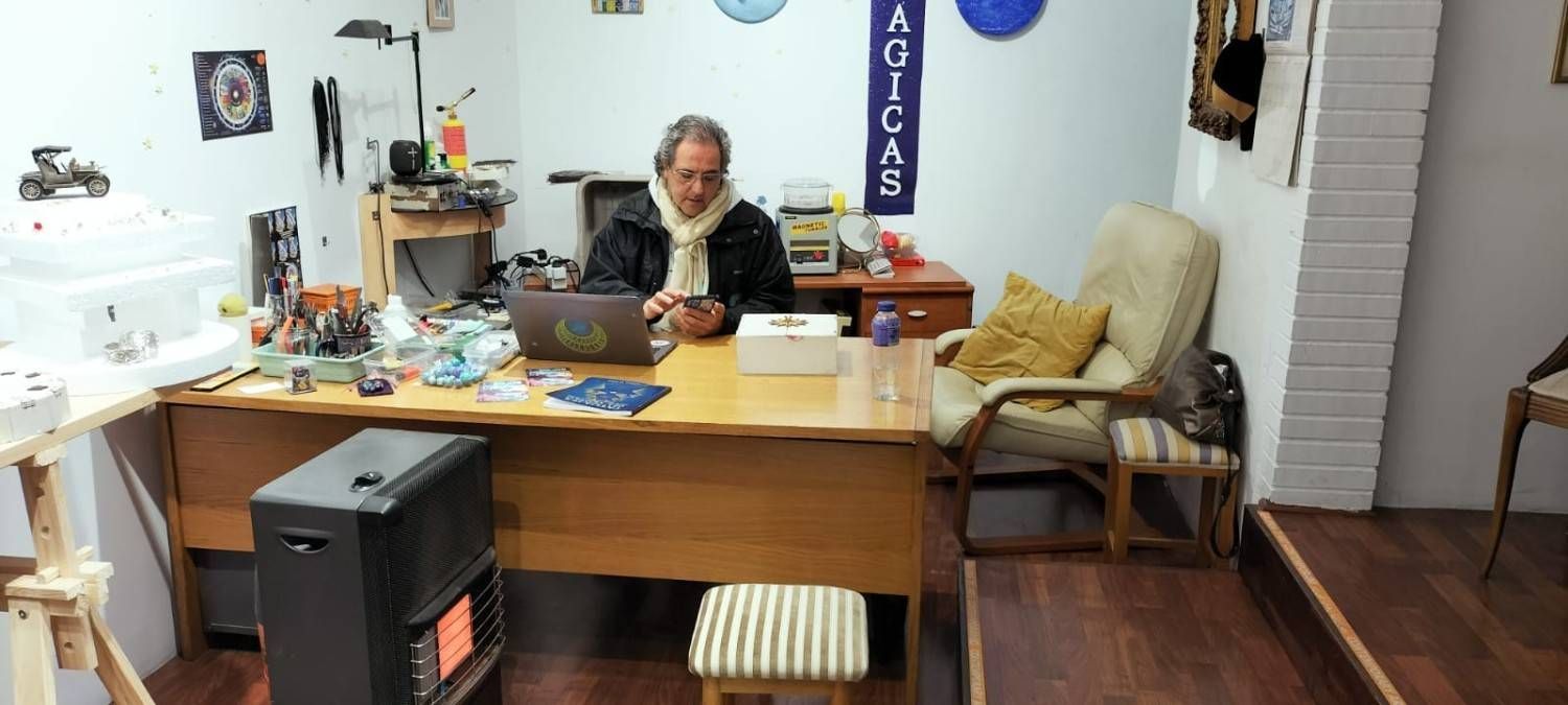 Persona sentada en un escritorio desordenado en una acogedora oficina en casa con papeles, plantas e iluminación cálida.