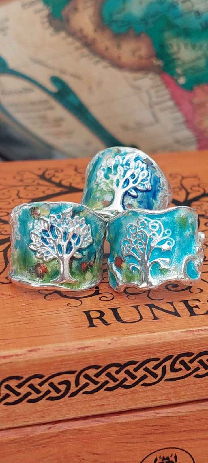 Tres dados de resina azul verdosa sobre una caja de madera tallada con runas y un borde decorativo de nudos.