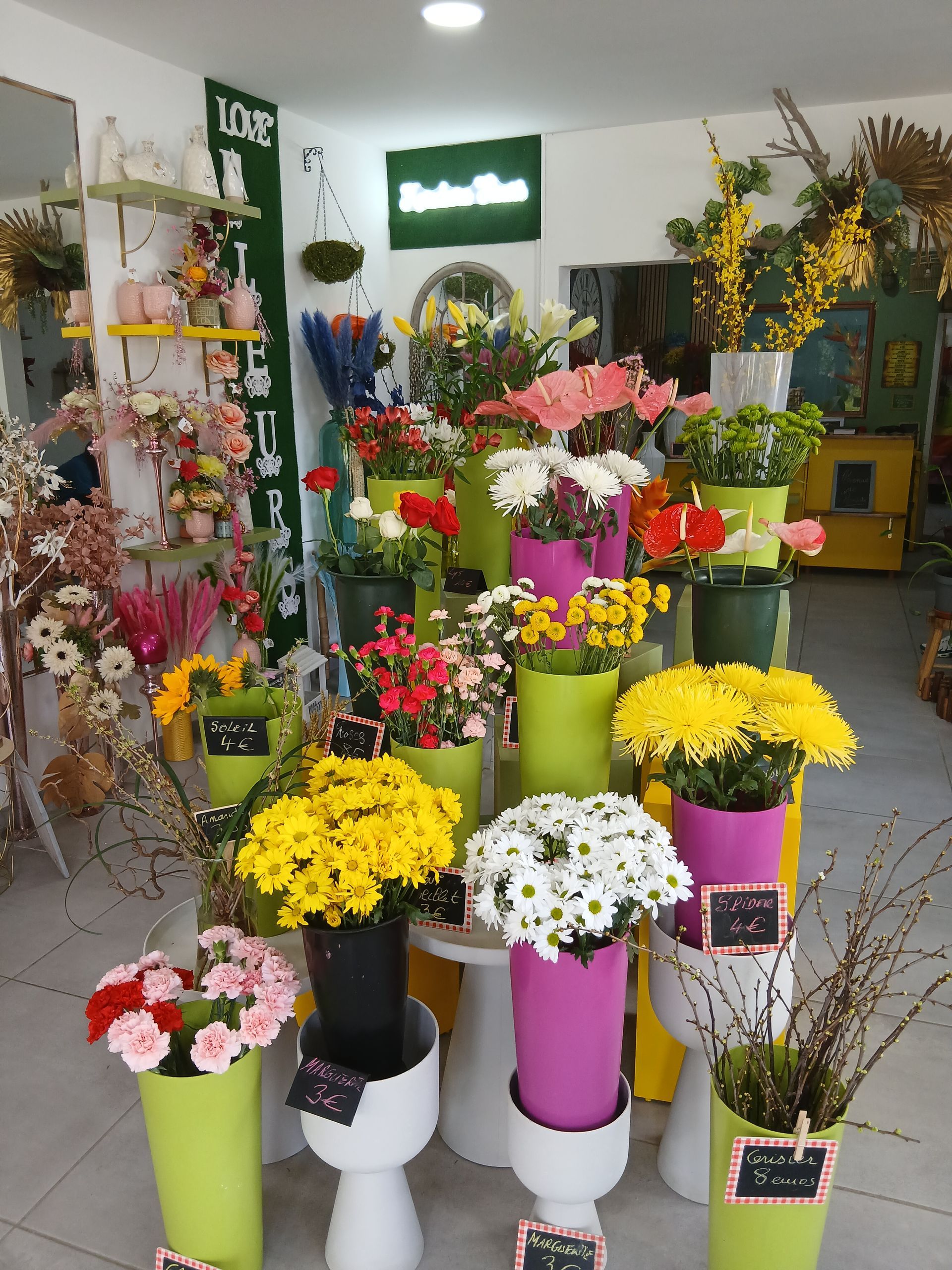 Présentoir de fleuriste : bouquets colorés dans des vases verts et roses, disposés sur des étagères.