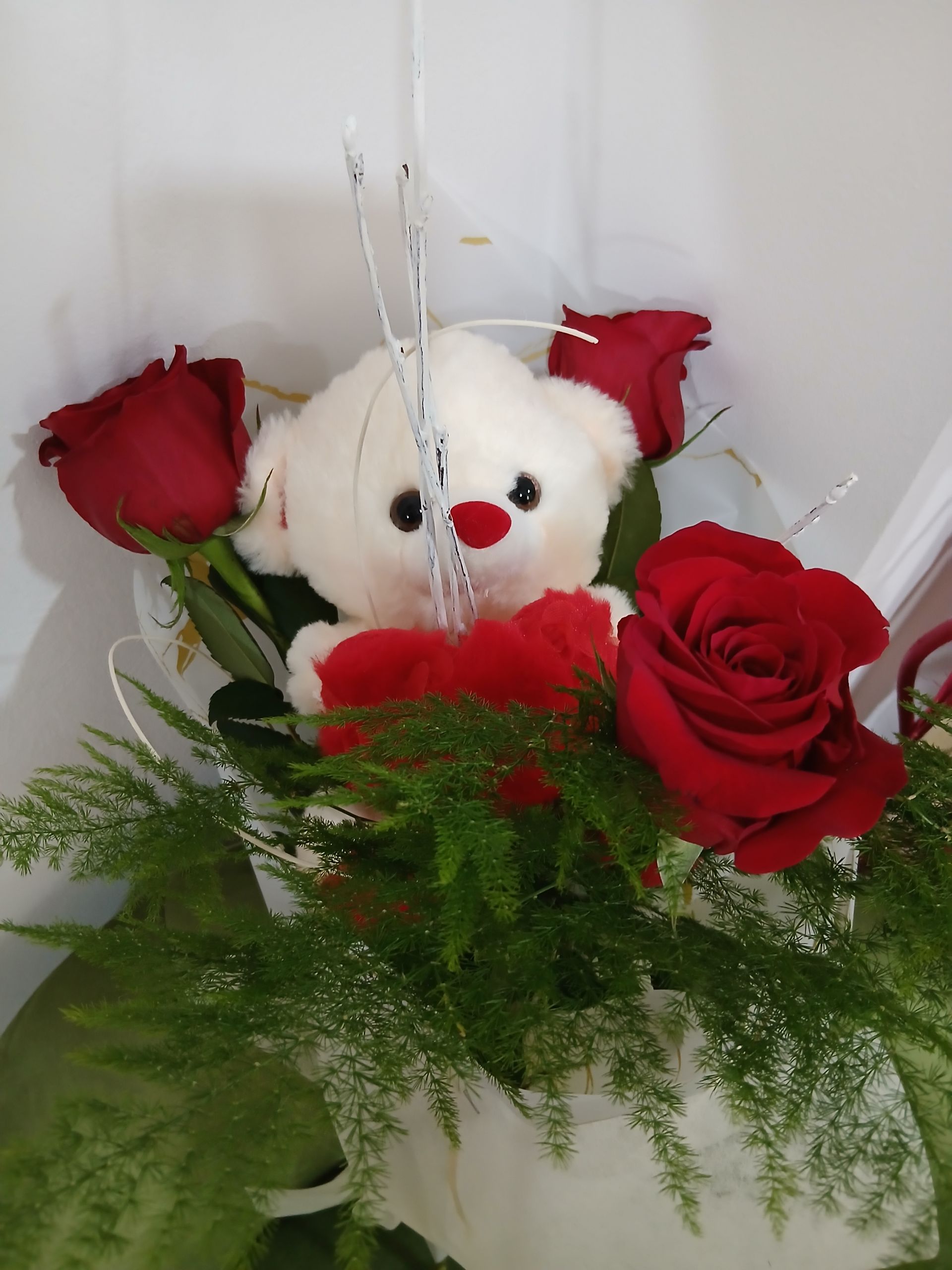 Un ours en peluche dans un bouquet de roses rouges et de verdure.