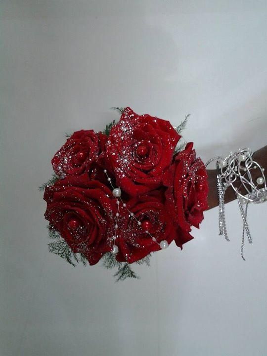 Bouquet de roses rouges orné de paillettes argentées et de perles, tenu par une main portant un bracelet en argent.