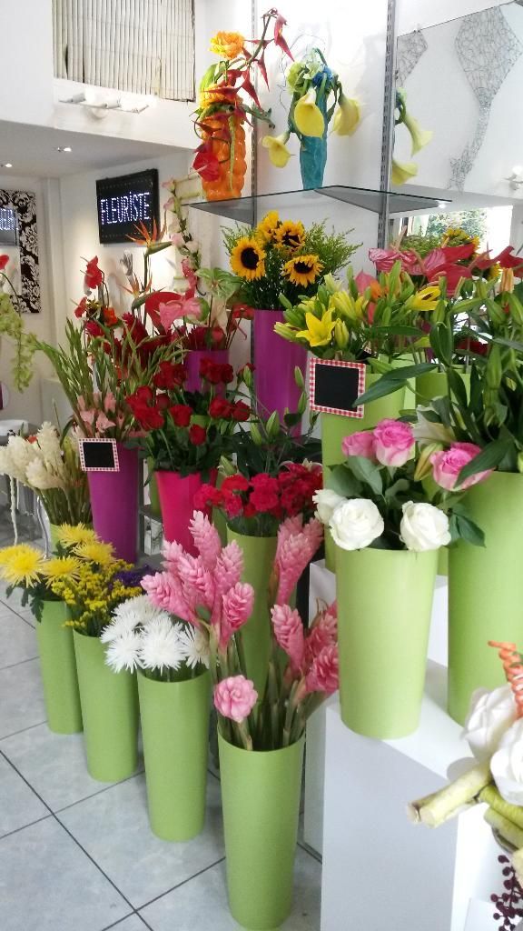 Présentoir de fleuriste : Bouquets colorés dans des vases verts et roses sur des étagères.