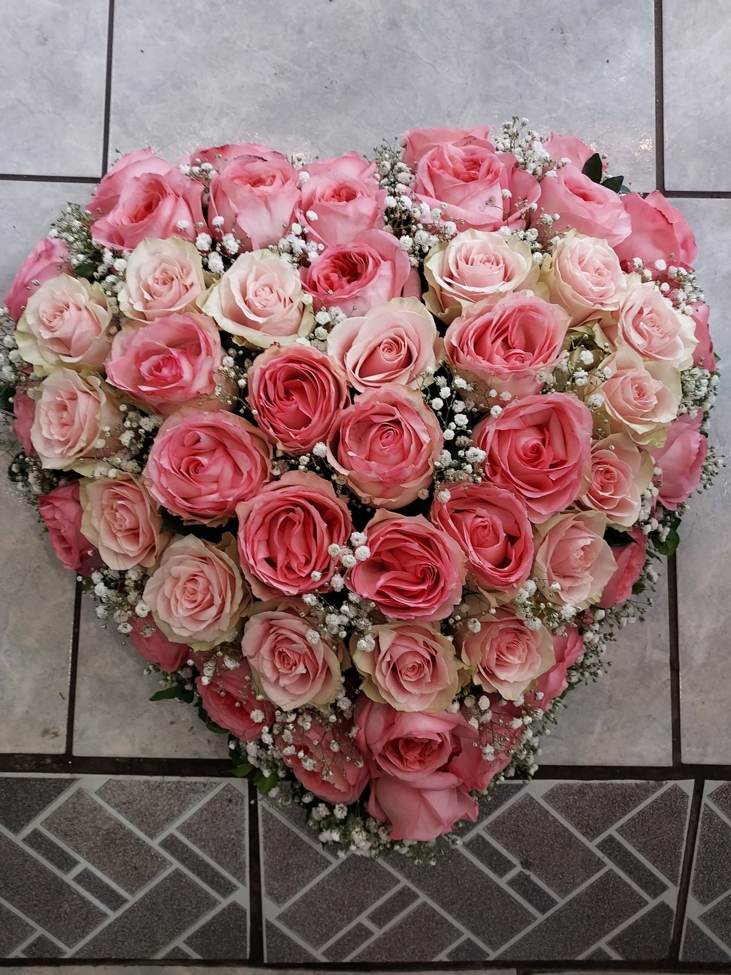 Composition en forme de cœur de roses roses et de gypsophile blanche sur une surface carrelée.