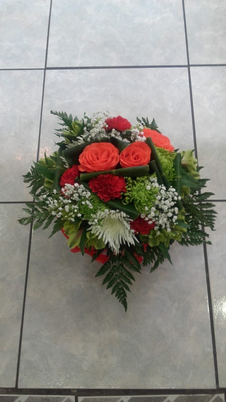 Composition florale avec roses orange, œillets rouges, fleurs blanches et feuillage vert sur carrelage.