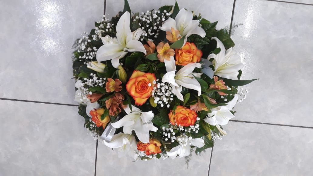 Couronne de lys blancs et de roses orange, avec de la verdure et de petites fleurs blanches.