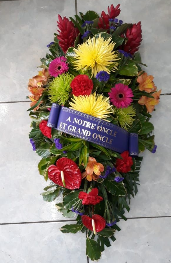 Gerbe funéraire de fleurs colorées avec un ruban bleu portant l'inscription « À notre oncle et grand oncle ».