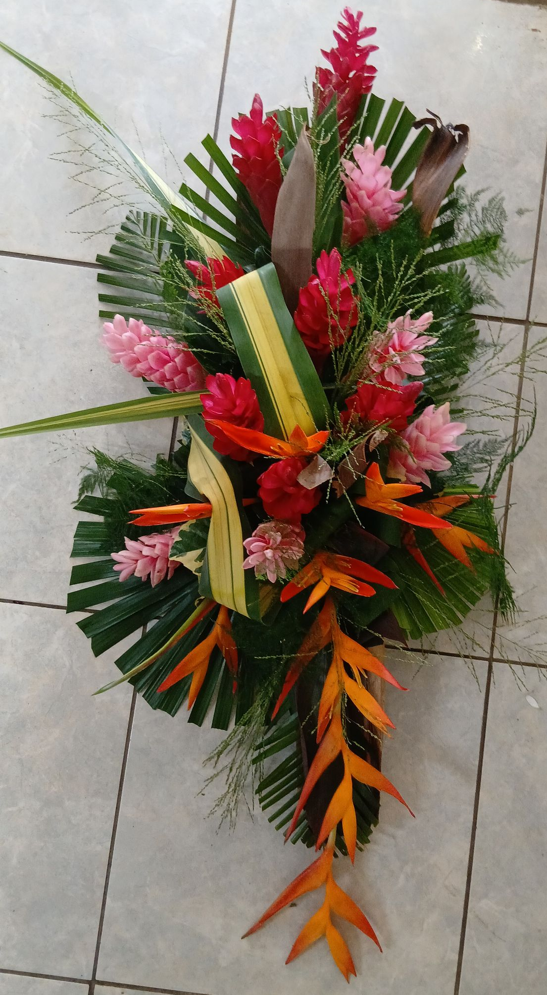 Une composition florale circulaire avec des lys blancs, des roses orange et du feuillage vert sur une surface carrelée.