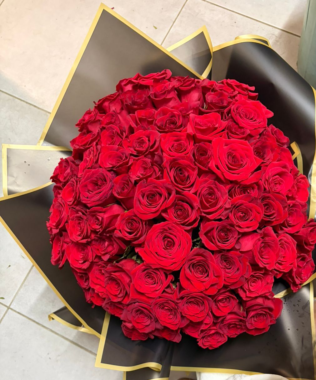 Bouquet de roses rouges enveloppé dans du papier noir à bordure dorée ; personne le tenant.