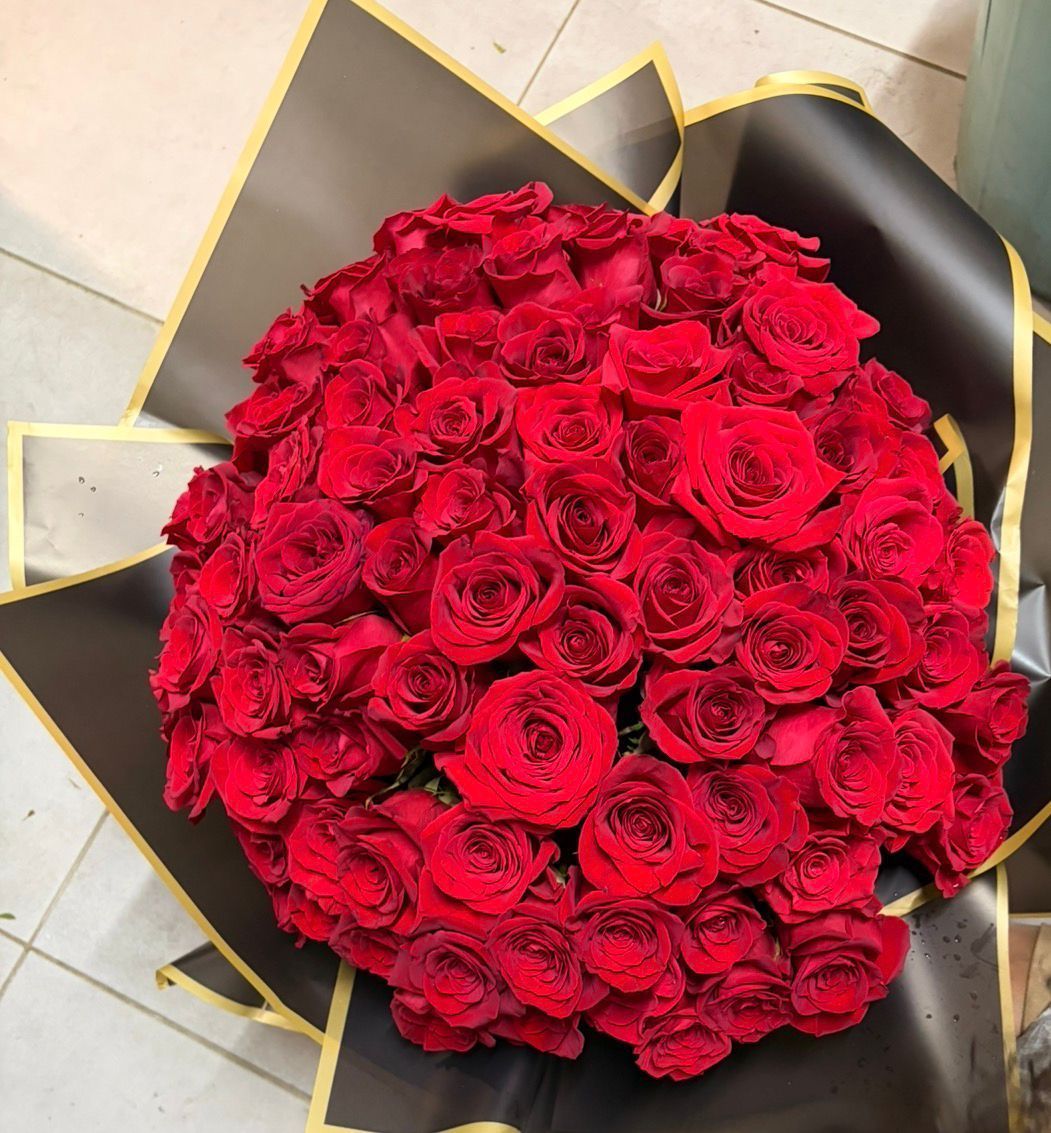Bouquet de roses rouges, enveloppé dans du papier noir à bordure dorée.