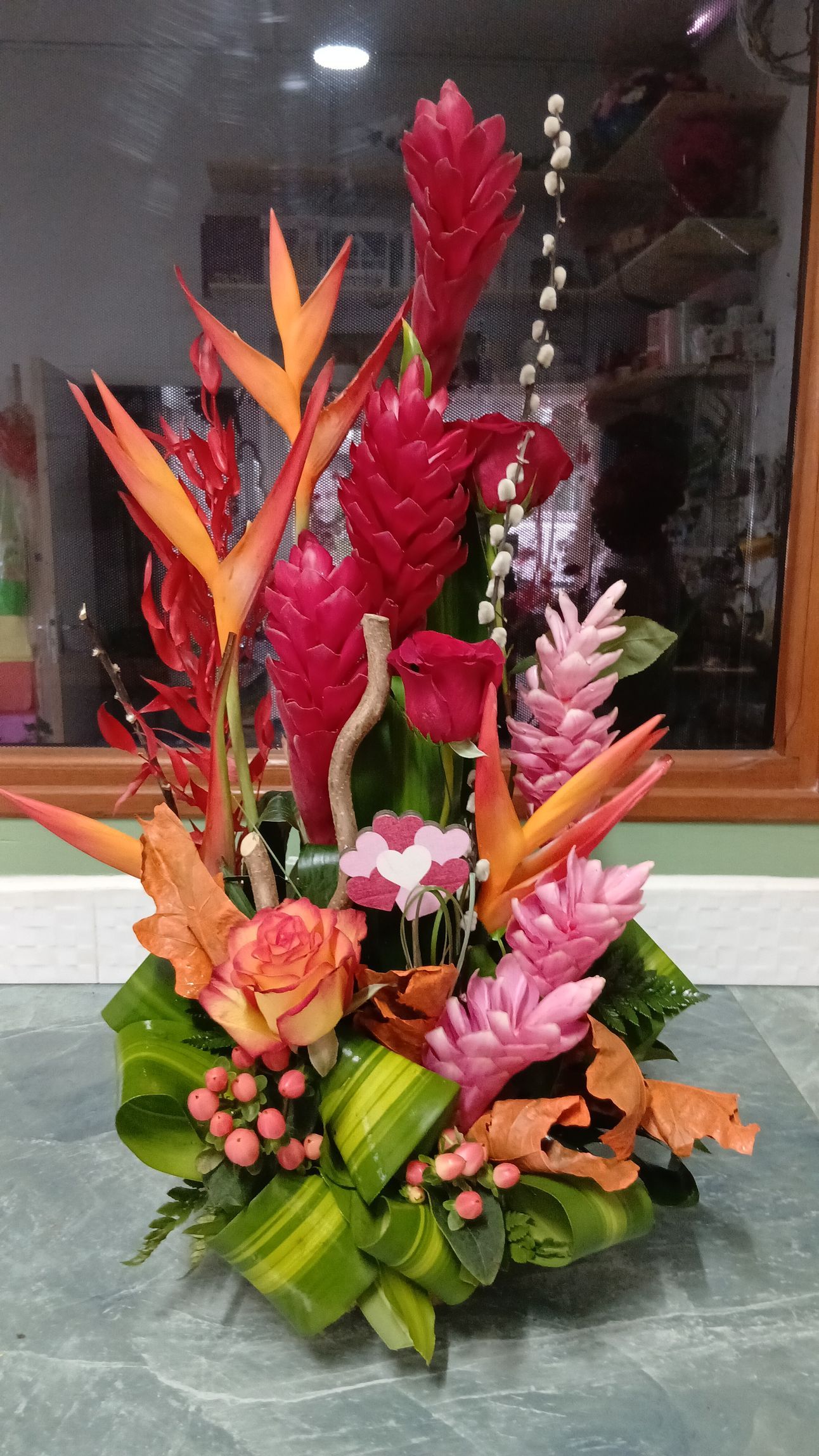 Composition florale tropicale aux couleurs vives orange, rose et rouge, disposée sur un fond vert bas.