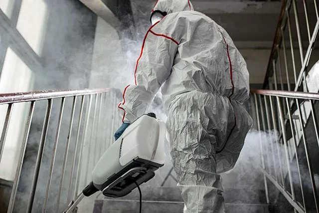 Eine Person in einem weißen Schutzanzug desinfiziert ein Treppenhaus. Bei der Schädlingsbekämpfung in Rostock desinfizieren wir Oberflächen, um Keime zu reduzieren.