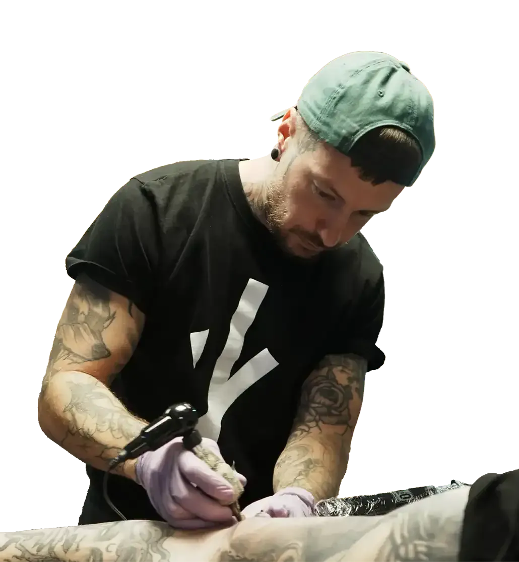 Eine Person mit grüner Kappe benutzt eine Tätowiermaschine, um ein Motiv auf die Haut einer anderen Person zu tätowieren.