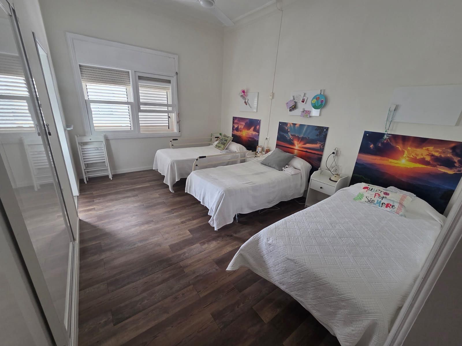 Tres camas con edredones florales rosas y verdes en un dormitorio muy iluminado, con muebles de madera.