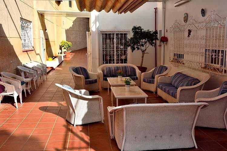 Patio exterior con muebles de mimbre blanco y suelo de baldosas rojas.