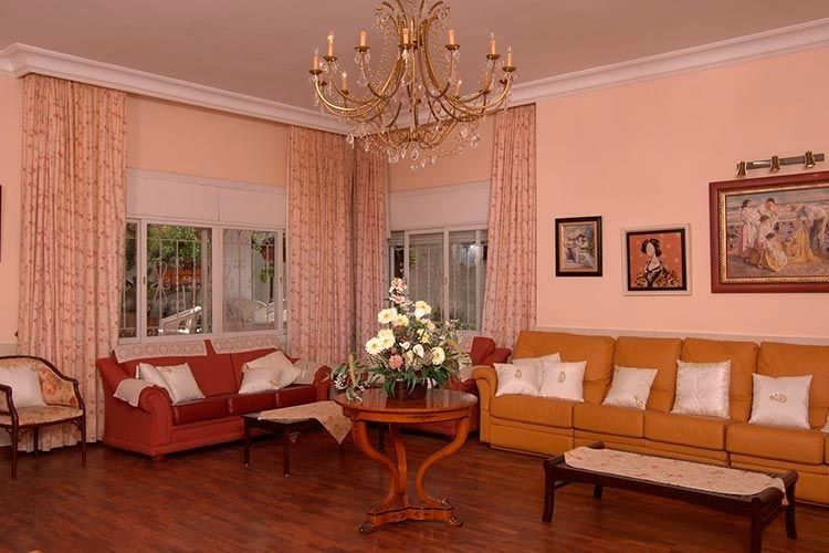 Sala de estar con paredes color melocotón, sofás rojos y amarillos, almohadas blancas y una lámpara de araña.