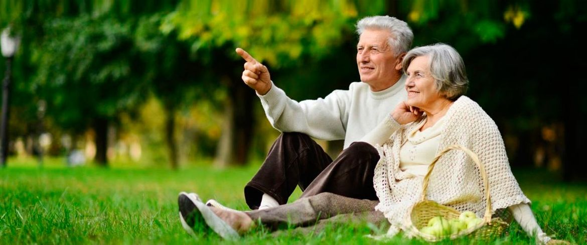 Una pareja de ancianos está sentada en el césped, mirando algo a lo lejos. El hombre señala.
