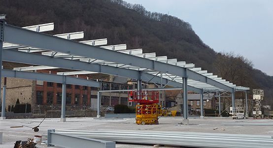 La structure métallique d'un bâtiment en construction, avec une montagne en arrière-plan. Un ascenseur jaune est visible.
