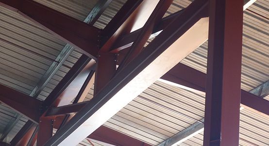 Poutres en acier rouge soutenant un toit en tôle ondulée.