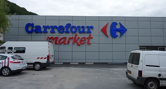 Façade du magasin Carrefour Market avec des camionnettes garées devant ; enseigne bleue et rouge.